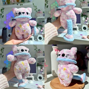 Op de afbeelding: Een handgemaakt pluche kattenknuffel in roze en wit, met gele sterren. Het heeft een blauwe kraag en een bijpassend blauw-wit gestreept accessoire. Het speelgoed is zacht en pluizig, met een grillig ontwerp.