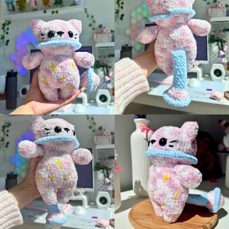 Op de afbeelding: Een handgemaakt pluche kattenknuffel in roze en wit, met gele sterren. Het heeft een blauwe kraag en een bijpassend blauw-wit gestreept accessoire. Het speelgoed is zacht en pluizig, met een grillig ontwerp.