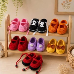 Könnte beinhalten: Eine Sammlung handgefertigter Häkel-Babyschuhe in verschiedenen Farben und Stilen, darunter rosa Mary Janes, schwarze Sneaker mit weißen Schnürsenkeln, orangefarbene Schuhe mit Perlenakzenten, rote Mary Janes, violette Schuhe mit Blumen und gelbe mit Schleifen.