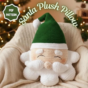 Könnte beinhalten: Ein gehäkeltes Santa Claus Plüschkissen mit grünem Hut, weißem Besatz und weißem Bart. Das Kissen ist beige mit rosigen Wangen und geschlossenen Augen. Die Worte "Santa Plush Pillow" sind über dem Kissen angeordnet.