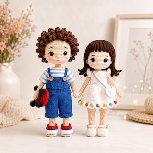 May include: Two handmade crochet dolls, a boy and a girl, stand side-by-side. The boy doll wears blue overalls, a striped shirt, and holds a red skateboard. The girl doll wears a white dress with a rainbow-colored hem and a heart-shaped purse.