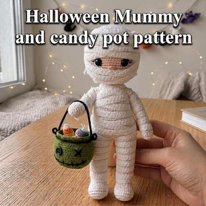 May include: A crocheted mummy doll wrapped in white yarn with large dark eyes, holding a small green crocheted candy pot with a black handle and stitched facial features. The text "Halloween Mummy and candy pot pattern" is visible above the doll.