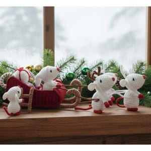 May include: A festive Christmas display featuring crocheted mice and a red sleigh. The mice are white with red noses and feet, some with antlers. The sleigh is red with brown runners, and the scene is decorated with greenery and ornaments.