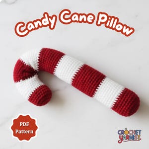 May include: A crocheted candy cane pillow in red and white stripes. The pillow is curved and has the words "Candy Cane Pillow" in red script. A PDF pattern is available.