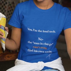 May include: A royal blue t-shirt with white and orange text that reads "Yes, I'm the lead tech. No- the 'man in charge' can't even find his own tools." A small illustration of pliers is below the text.