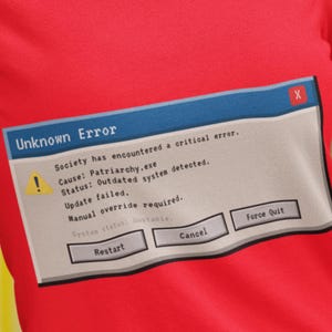 Può includere: Una maglietta rossa con un messaggio di errore del computer. Il messaggio, in una finestra blu, recita "Unknown Error" e descrive un errore di sistema dovuto a "Patriarchy.exe". I pulsanti includono "Restart", "Cancel" e "Force Quit".