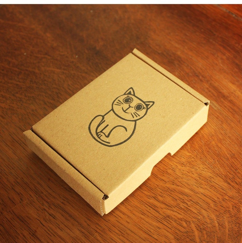 May include: A brown cardboard box with a cartoon cat illustration on the front. The cat is black and white and has a smiling face.