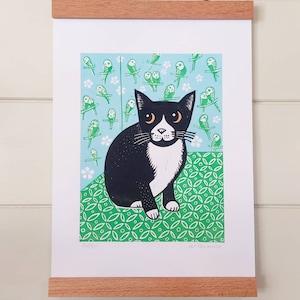 May include: A black and white cat with green eyes sits on a green patterned background. The cat is surrounded by green birds on a light blue background. The print is signed "Sally" and "G.T. Kendall".