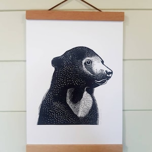 May include: A black and white illustration of a sun bear's head and shoulders, printed on a white background and framed with a natural wood frame.