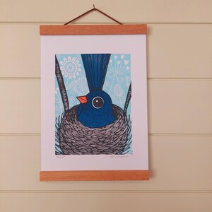 May include: A blue bird with a black and white nest, surrounded by a light blue background with white flowers and leaves. The bird has a large black eye and an orange beak. The print is titled "The Nest" and signed "Lot Emerson".