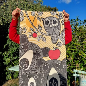 May include: A colorful fabric panel with a black and white owl, red apples, and three black bears with white accents. The bears have large eyes and are arranged in a vertical stack.