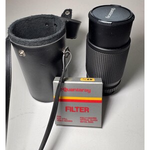 May include: A black Quantaray camera lens with a matching lens cap and a black leather case. A silver and grey filter box with the word "FILTER" in red and the Quantaray logo is also present.