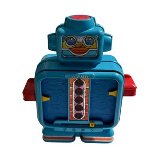 May include: A vintage toy robot in shades of blue, red, and yellow. The robot has a boxy body with a face-like design on the head. The word "ALPHIE" is printed on the front. The robot has a retro aesthetic.