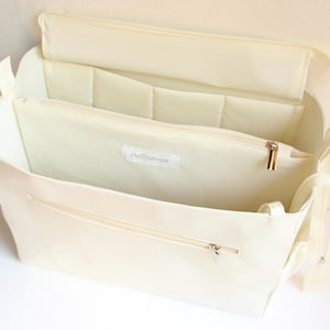 Op de afbeelding: Een witte canvas tote bag met meerdere binnenzakken en een ritssluiting. De tas heeft een label met de tekst "daffy dream".
