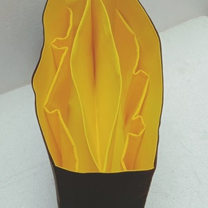May include: A yellow fabric organiser with multiple compartments, folded into a compact shape. The organiser is made of a soft, pliable material and has a black base.