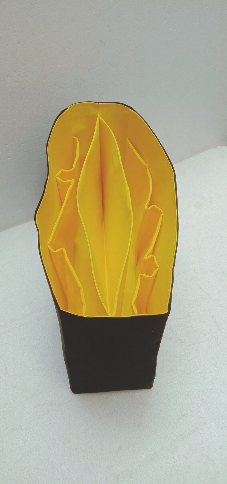 May include: A yellow fabric organiser with multiple compartments, folded into a compact shape. The organiser is made of a soft, pliable material and has a black base.