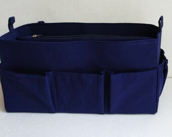 May include: A navy blue felt bag organizer with multiple pockets and handles. The organizer has a zippered top and several exterior pockets for storage. A small white tag with a logo is attached to the side.