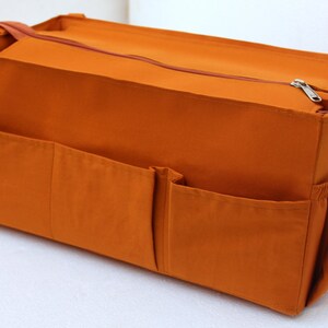 May include: A brown canvas organizer with multiple pockets and a zipper closure. The organizer is designed to fit inside a larger bag.