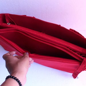 May include: Red fabric tote bag with multiple compartments and zips. The bag is open and the interior is visible.