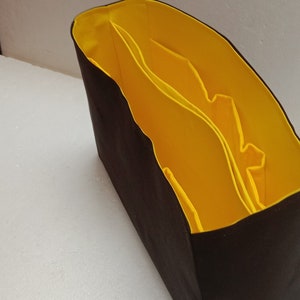 May include: A black fabric organiser with a yellow lining and multiple compartments. The organiser is designed to fit inside a larger bag.