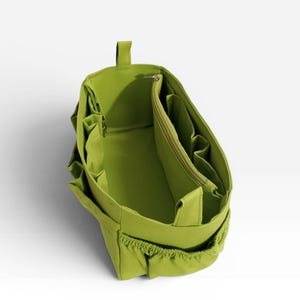 Op de afbeelding: Een limoengroene tasorganizer met een gestructureerde rechthoekige vorm, voorzien van meerdere binnen- en buitenzakken, een centraal vak met ritssluiting en een handvat aan de bovenkant om spullen in een grotere tas te ordenen.