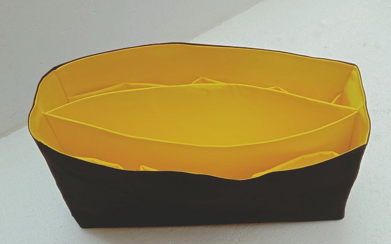 May include: A black fabric organiser with a yellow lining and multiple compartments. The organiser is designed to fit inside a larger bag.