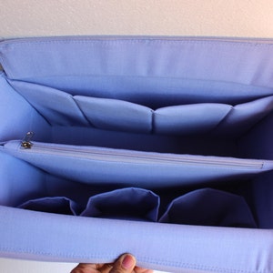 Op de afbeelding: Een lichtblauwe stoffen organizer met meerdere vakken en een ritsvak. De organizer heeft een zacht, gevoerd interieur en is ontworpen om in een grotere tas te passen.