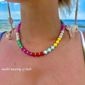 Pode incluir: Um colar de contas coloridas com um arco-íris de tons, incluindo rosa, verde, amarelo e azul, é exibido. O colar tem aproximadamente 43 cm de comprimento. Distanciadores dourados separam as contas. O texto "model wearing 17 inch" é visível.