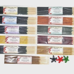 Könnte beinhalten: Eine Auswahl an Räucherstäbchen in verschiedenen Farben, jeweils in durchsichtigem Kunststoff verpackt. Die Etiketten auf den Verpackungen zeigen den Markennamen "Shrimp-Lallies" sowie Produktnamen. Drei kleine, sternförmige Kunststoffobjekte in Schwarz, Rot und Grün befinden sich unten.