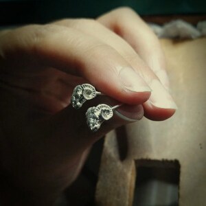 Peut inclure: Une paire de boucles d'oreilles en argent avec un design unique présentant une forme organique texturée. Les boucles d'oreilles sont tenues dans une main, mettant en valeur leurs détails complexes.