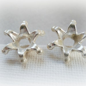 May include: Two silver star-shaped earring settings with a round center hole for a gemstone.