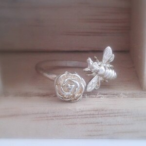 Peut inclure: Une bague en argent avec un motif d'abeille et de rose. L'abeille est perchée sur la rose, qui est détaillée avec des pétales texturés.