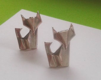 May include: A pair of silver origami cat earrings. The cats are folded in a traditional style and have a simple, elegant design.