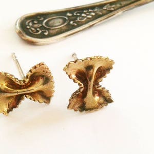May include: A pair of gold-toned earrings shaped like pasta. The earrings are small and delicate, and they would make a great gift for a food lover.