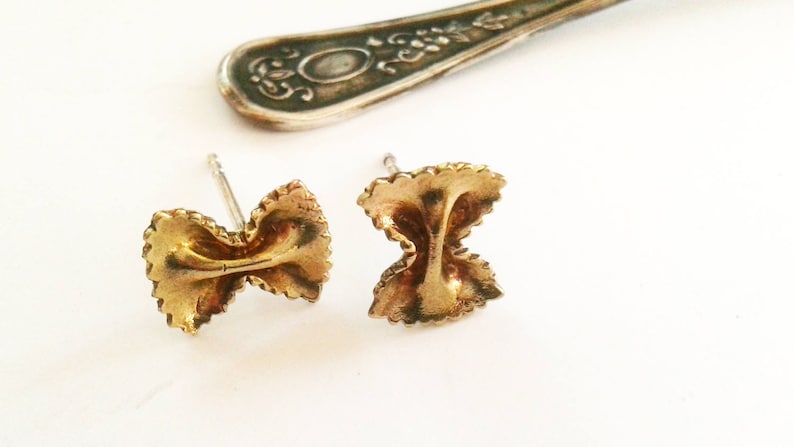 May include: A pair of gold-toned earrings shaped like pasta. The earrings are small and delicate, and they would make a great gift for a food lover.
