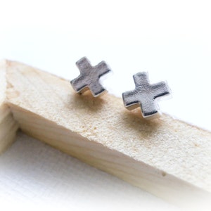 May include: A pair of silver cross-shaped stud earrings. The earrings are small and delicate, and they are perfect for everyday wear.