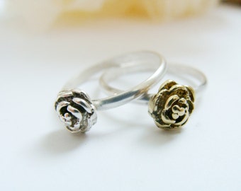 May include: Two silver rings with rose-shaped designs. One ring has a silver rose, and the other has a gold rose.