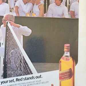 May include: An advertisement for Johnnie Walker Red Label Scotch whisky. The image shows a tennis match with spectators and the text "your set, Red stands out."