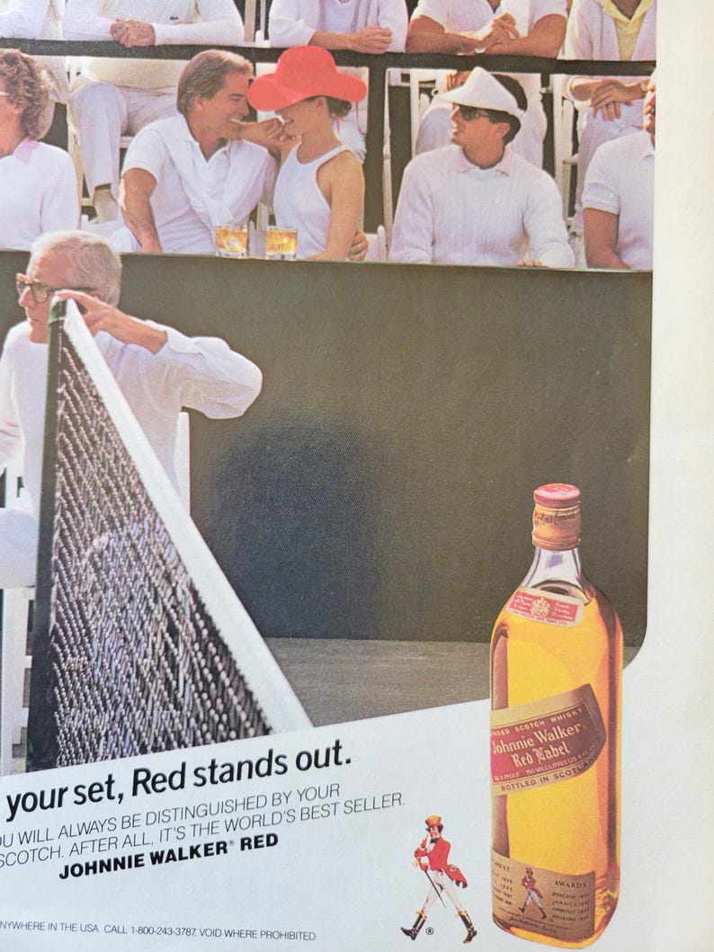 May include: An advertisement for Johnnie Walker Red Label Scotch whisky. The image shows a tennis match with spectators and the text "your set, Red stands out."