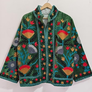 May include: A green velvet jacket with colorful floral embroidery. The jacket features a high collar, a zipper closure, and is adorned with red, yellow, blue, and gray flower designs. The lining has a striped pattern.