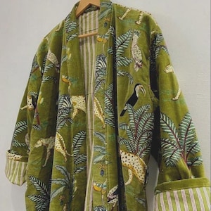 May include: Green velvet robe with a jungle-themed pattern featuring leopards, toucans, and zebras. The robe has a striped lining and cuffs, and is hanging on a wooden hanger.