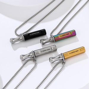 May include: Four necklaces with pendant-style accessories. The pendants are rectangular with a cylindrical mouthpiece and are in black, rainbow, silver, and gold. Each pendant has the text "5x20PRO MAX" printed on it. The necklaces have a silver chain.
