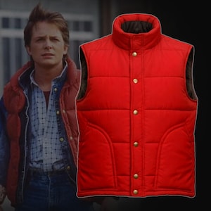 Puede incluir: Un chaleco acolchado rojo brillante con cuello alto y botones dorados. El chaleco tiene un diseño clásico y abultado, con un forro interior marrón oscuro. Esta prenda de abrigo es una elección de moda popular.