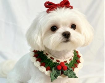 May include: A white Maltese dog wearing a red bow and a crocheted collar. The collar is decorated with green leaves, red berries, and white scalloped edges, creating a festive holiday look.