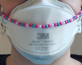 May include: A white 3M Aura 1863+ respirator mask with a beaded chain. The chain features pink, blue, and white beads. The mask has the text "3M Aura 1863+" printed on it.