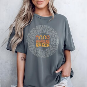 A woman wearing a gray t-shirt with the text "DANCING QUEEN" printed on it.