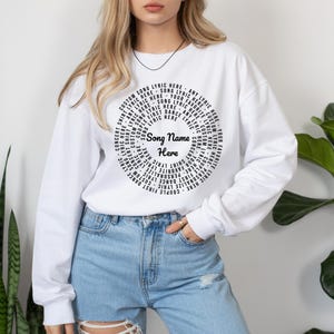 May include: White sweatshirt with a circular design featuring song lyrics and the text "Song Name Here." The design includes phrases like "Custom Song Lyric Here" and "First Dance Lyric Here."