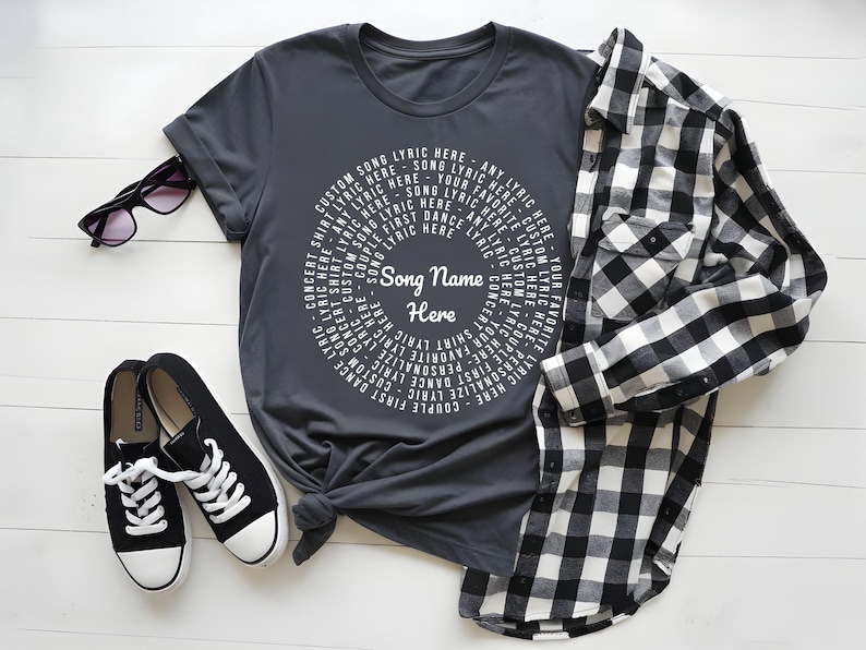 A gray t-shirt with a white circular design, a pair of black and white sneakers, and a black and white plaid shirt are arranged on a white surface.