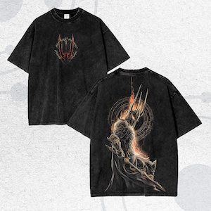 May include: Black t-shirt with a distressed wash. The front features a red and gold graphic. The back displays a detailed illustration of a figure with a crown and a fiery background. The shirt has short sleeves and a crew neck.