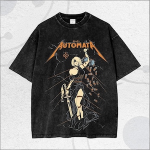 May include: Black, oversized t-shirt featuring the text "AUTOMATA" in orange, with a graphic of a female character holding a sword. The design has a distressed, vintage look. The shirt is made of a soft, comfortable material.